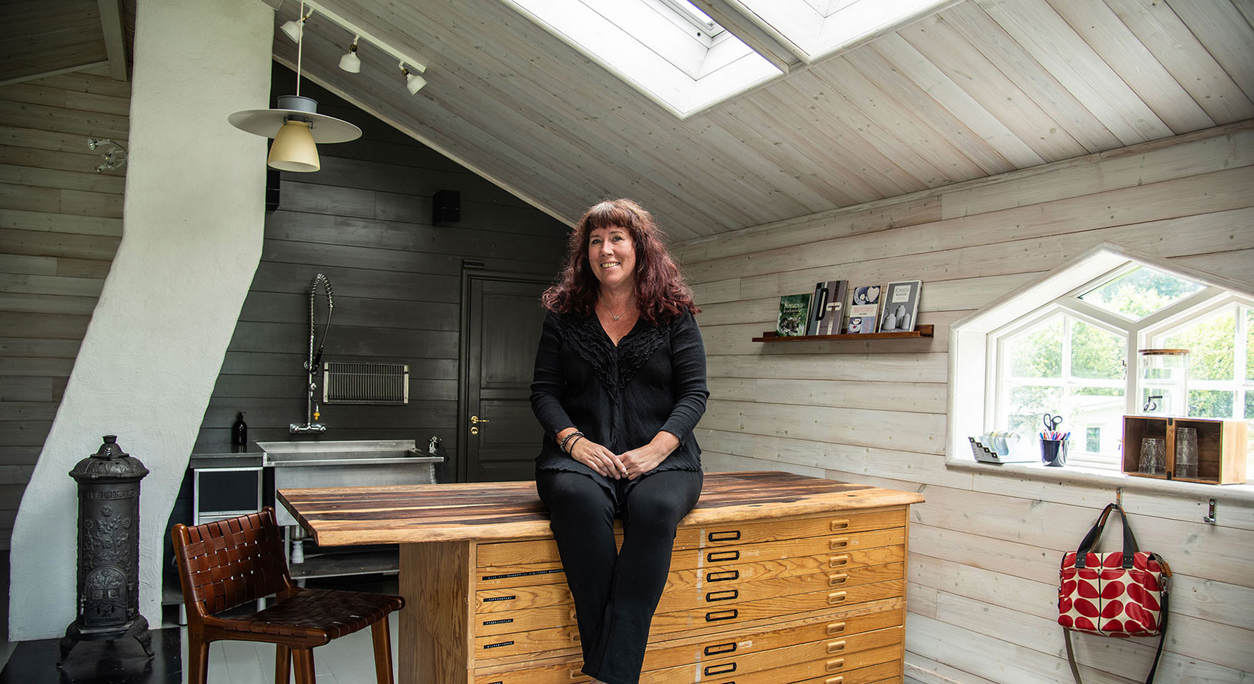 Mari Forsell, grafisk formgivare, sittande på en bänk i sin ateljé